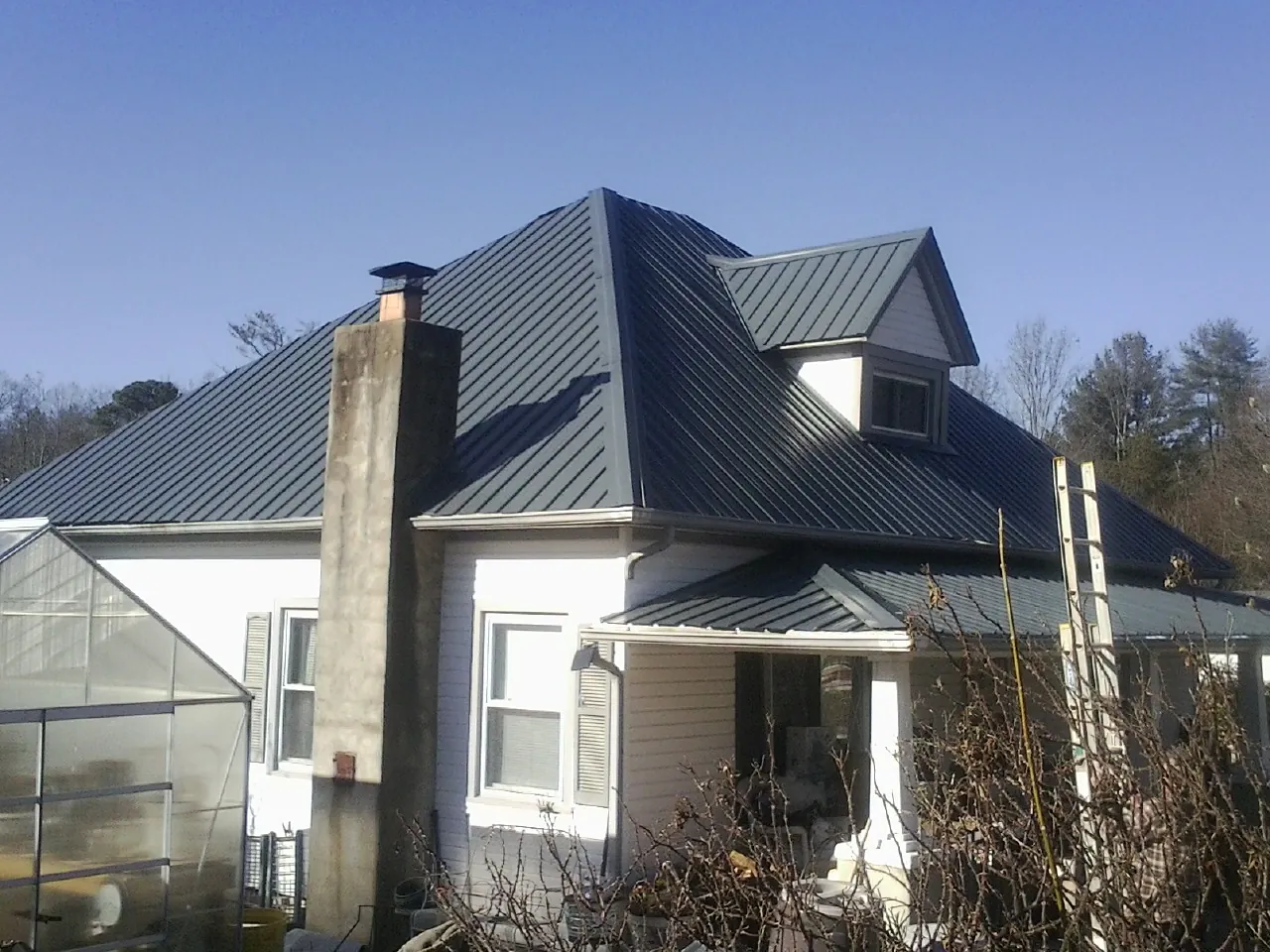 Dark blue standing seam metal roof on a white farmhouse with dormer — Slate & Tile Roof Repair by Roofing Brothers in Lee