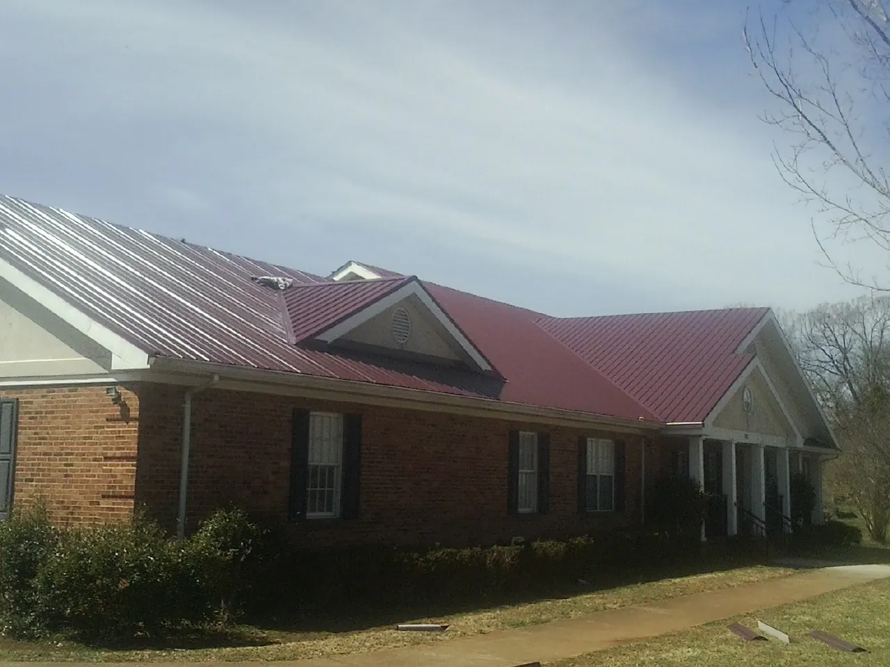 Red metal roof with gabled entries on a long brick building, from a Hail Damage Roof Repair job in Lee