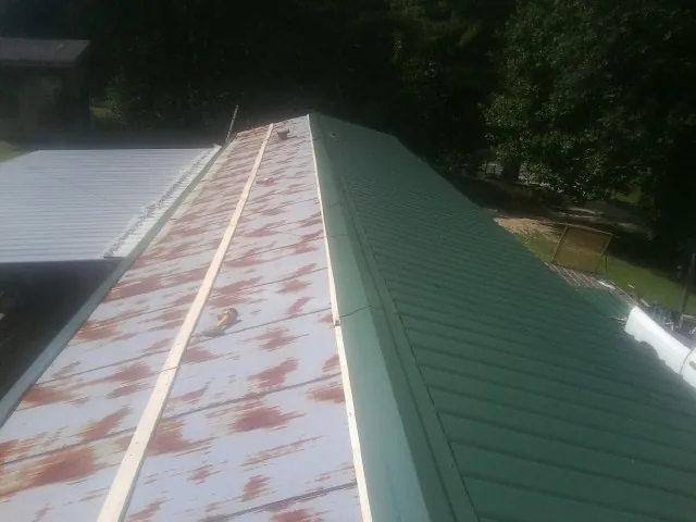 Old rusted panels beside newly installed green metal roofing — Wind Damage Roof Repair by Roofing Brothers in Lee