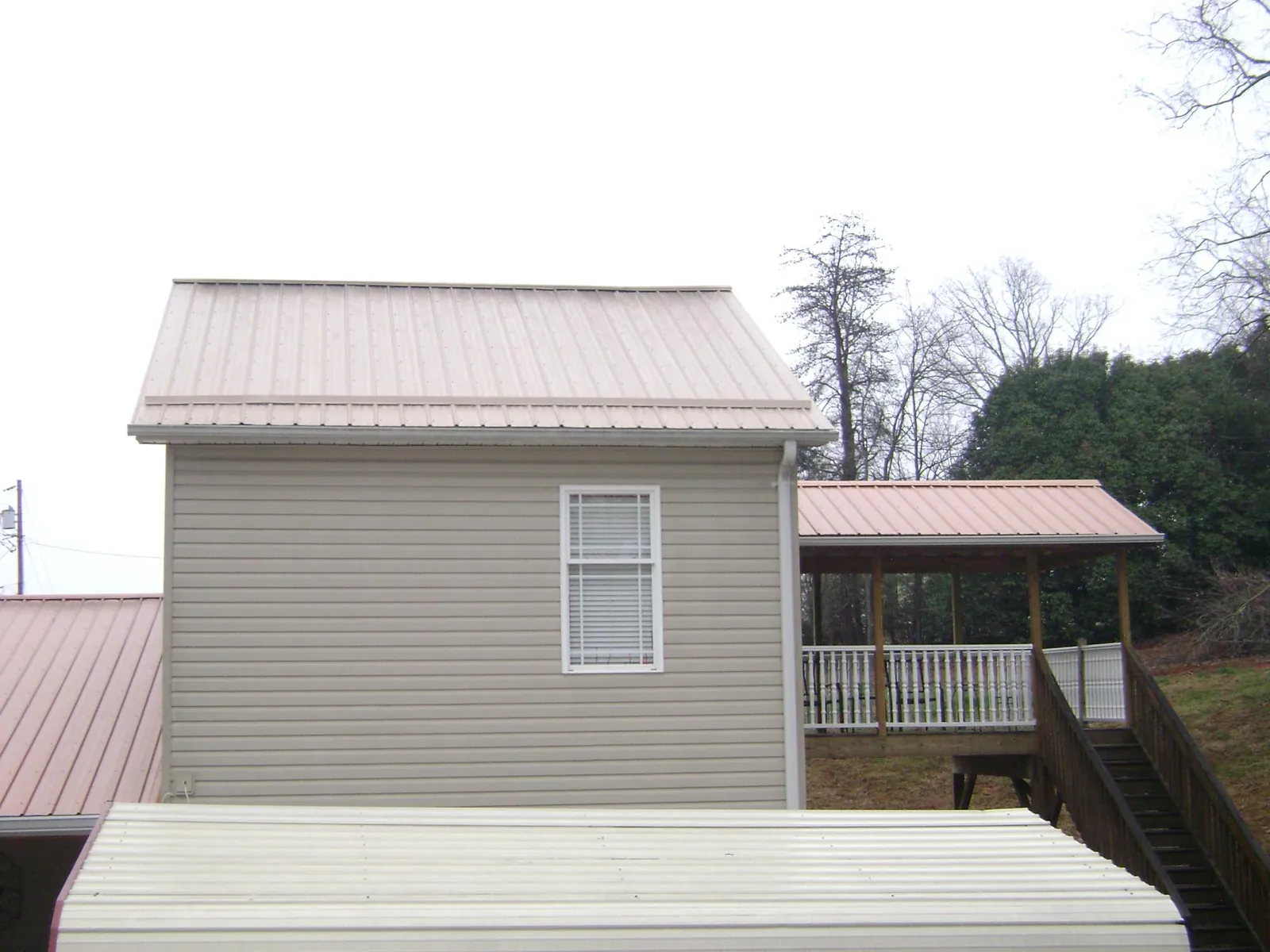 Tan metal roofs on a two story addition and attached porch, from a Roof Replacement job in Lee